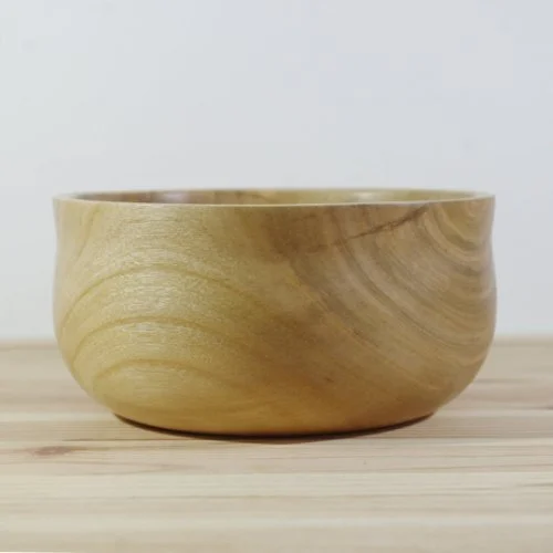 A wooden bowl on a light wooden surface against a plain white background.