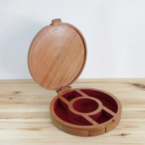 Round wooden jewellery box with a hinged lid and red velvet-lined compartments, placed on a wooden surface.