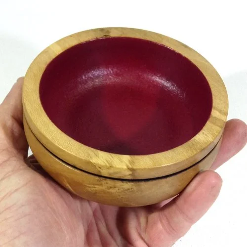A hand holding a small wooden bowl with a red interior.