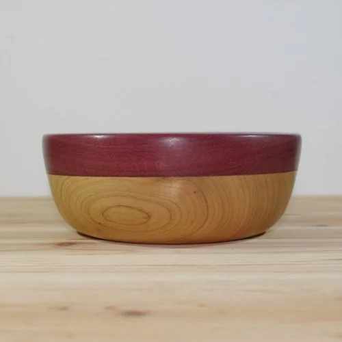 A wooden bowl with a red rim placed on a light wooden surface.