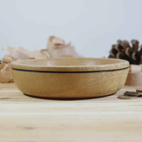 A round wooden bowl on a light wooden surface with decorative elements and pinecones in the background.