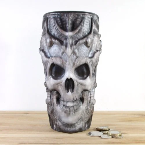 A skull-shaped wooden vase inspired by H.R.Giger, placed on a wooden surface next to some coins.