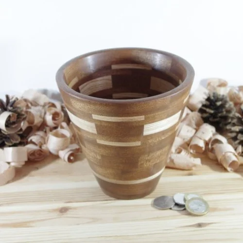 A segmented wooden vase , placed on a wooden surface with coins nearby, surrounded by decorative wood shavings.