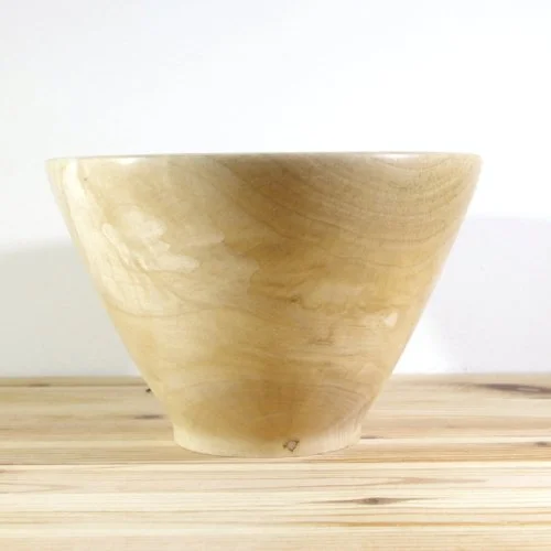 A wooden bowl on a light wooden surface against a white background.