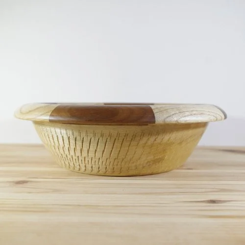 A wooden bowl with a decorative rim resting on a light wooden surface.