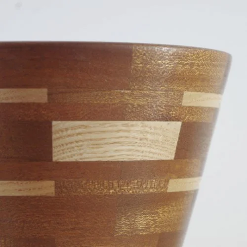 Close-up of a segmented wooden vase with alternating light and dark horizontal wood grain patterns.