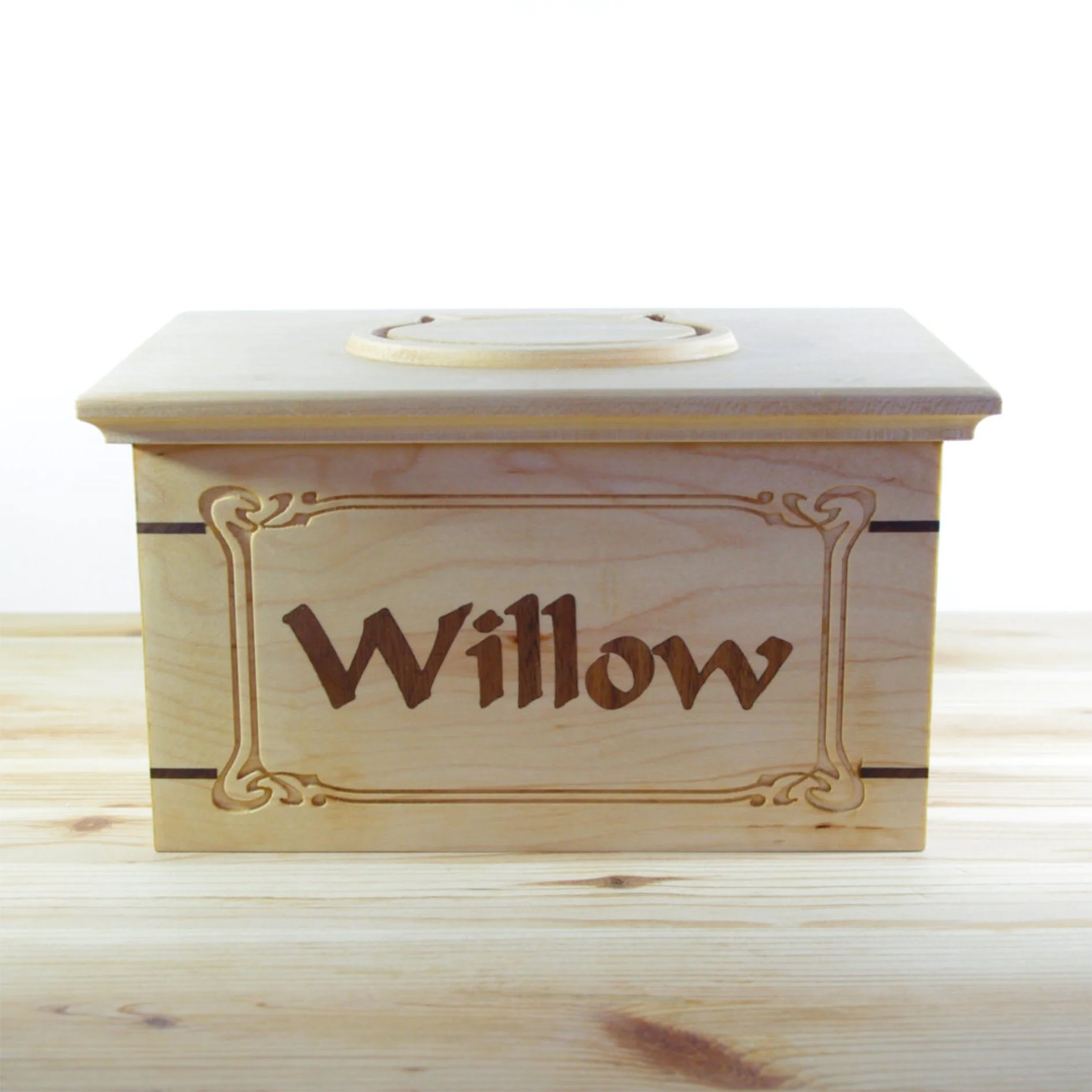 A pet urn with the word 'Willow' engraved on the front, sitting on a wooden surface.