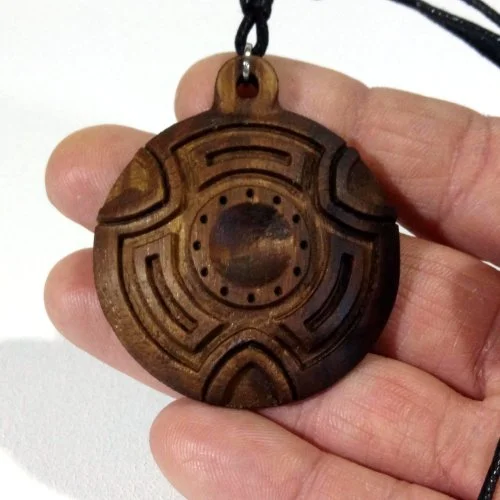 A round wooden pendant with carved geometric patterns, attached to a black cord.