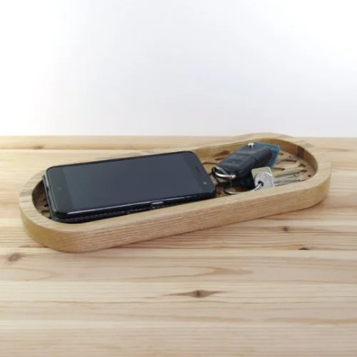 A black smartphone and car key fob inside a wooden tray on a light wooden surface.