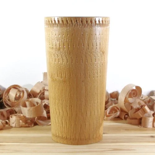 Wooden vase with wood shavings scattered around it on a wooden surface.
