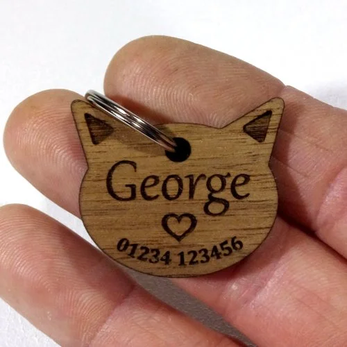 Wooden pet tag shaped like a cat's head with the name George, a heart, and phone number, attached to a keyring.