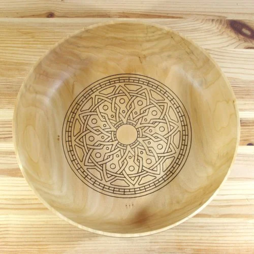 Wooden bowl with intricate geometric pattern etched inside, resting on a wooden surface.