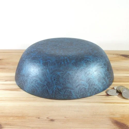 A blue wooden bowl on a wooden surface with some coins beside it.