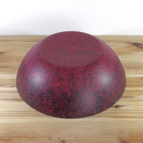 A round, dark red and black patterned bowl or container placed upside down on a wooden surface.
