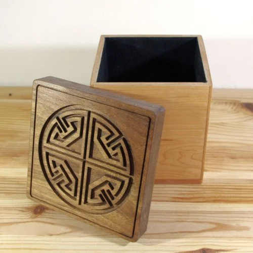 A wooden box with a removable lid that has a carved circular design on top, placed on a wooden surface.