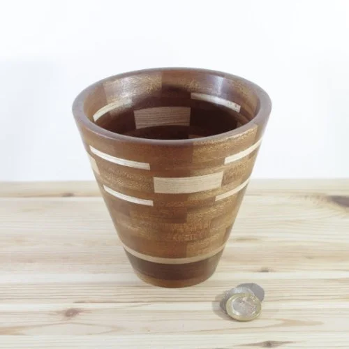 A segmented wooden vase with horizontal striped pattern next to a quarter on a light wooden surface.