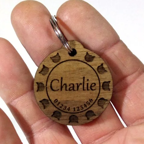 Wooden cat tag engraved with the name Charlie and paw prints around the edge.