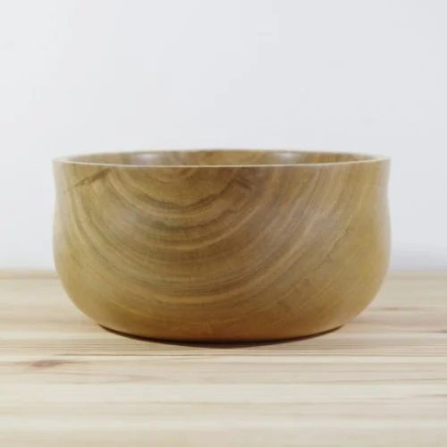 A wooden bowl on a light wooden surface with a white background.
