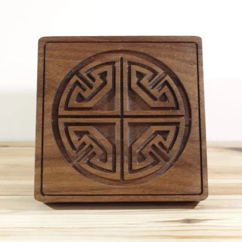 A wooden keepsake box lid with intricate circular geometric carvings on its front face, resting on a wooden surface.