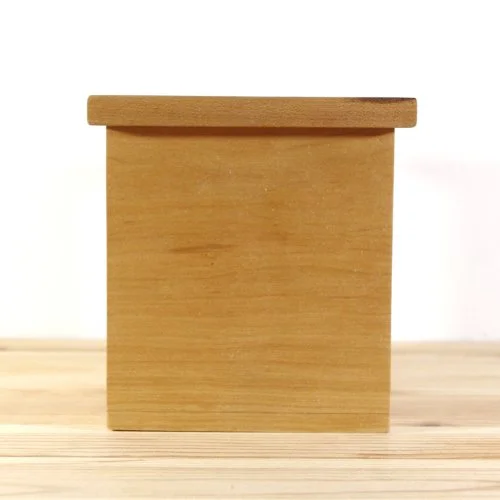 A small wooden box with a flat top, placed on a light wooden surface against a white background.
