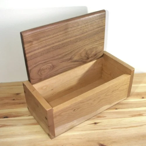 Ash wooden storage box with a hinged Walnut lid, open to show the empty interior, placed on a wooden surface.