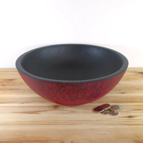 Red and black decorative bowl with coins on wooden surface.