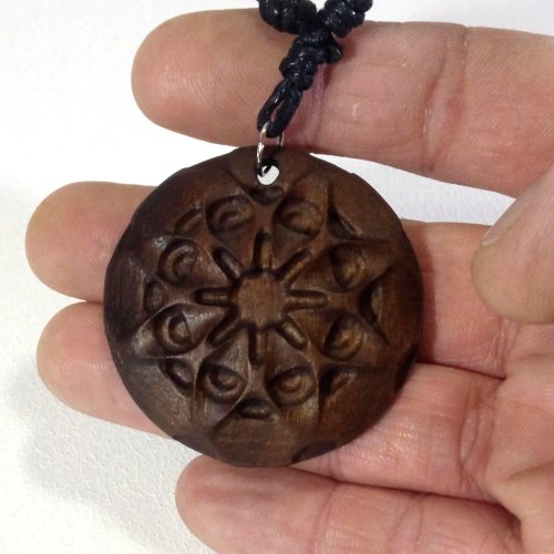 A person holding a round wooden pendant with carved geometric patterns on it, attached to a black beaded necklace.