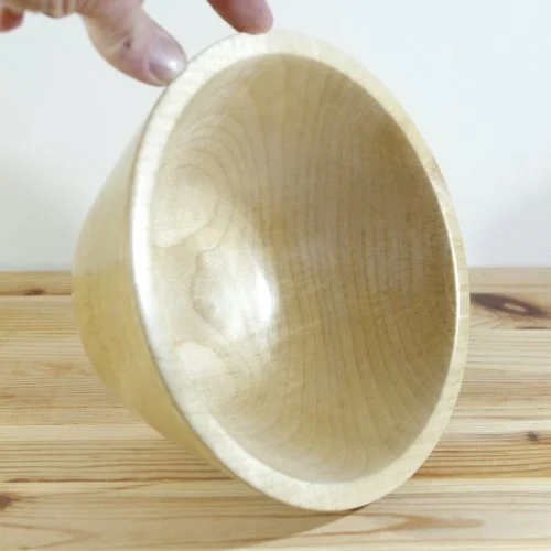 A hand holding a wooden bowl over a wooden surface.