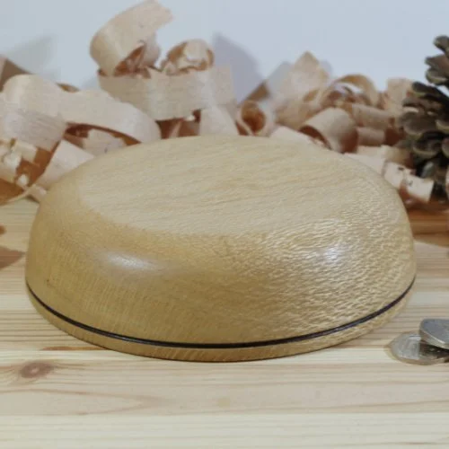 A wooden bowl on a wooden surface, with wood shavings and pinecones in the background.