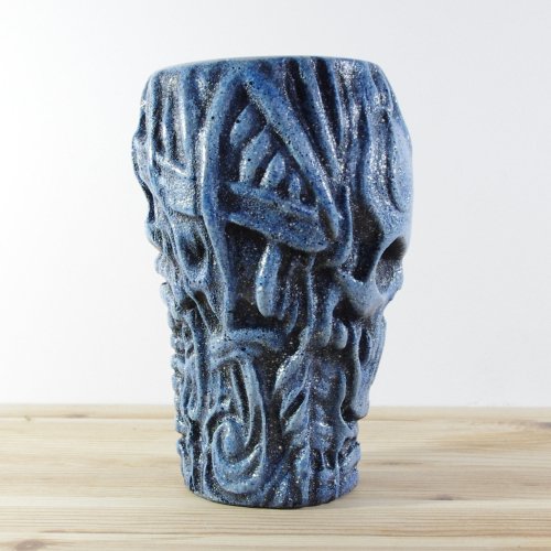 A wooden vase  with a textured surface, blue and black, featuring a carved skull and abstract patterns.