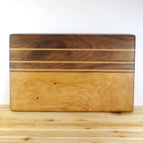 Maple and Walnut chopping board with three light-colored stripes on a darker wood background, sitting on a wooden surface.