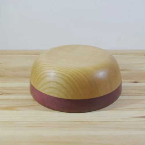 A small, rounded wooden bowl with a natural wood top and a darker wood rim, placed on a light wooden surface.