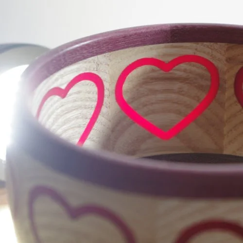 Close-up of a container with red heart patterns on a beige background with a purple rim.