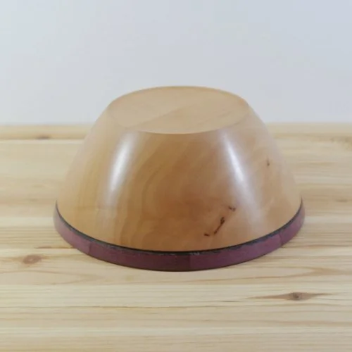 A steamed pear wooden bowl with a purple heart rim, placed upside down on a light wooden surface.