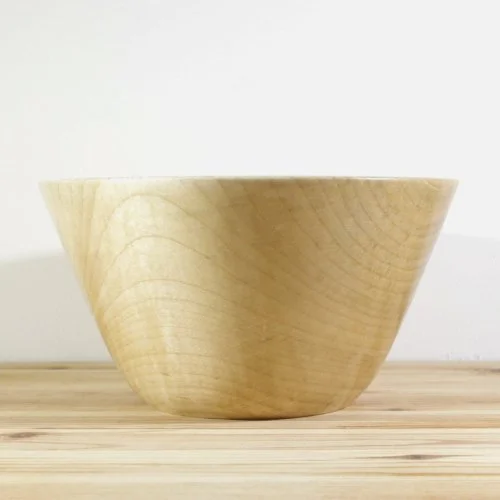 A wooden bowl placed on a wooden surface with a plain white background.