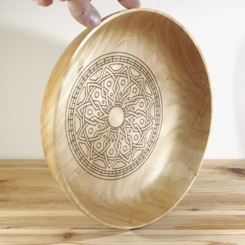 A wooden bowl with an intricate circular geometric pattern engraved on the inside.
