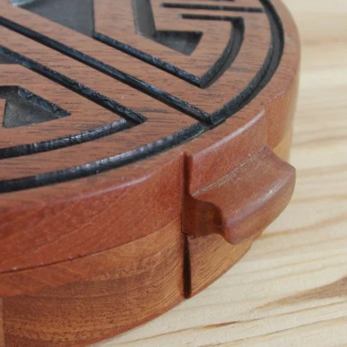 Close-up of a wooden jewellery box with a black design, showing a small wooden handle on the side.