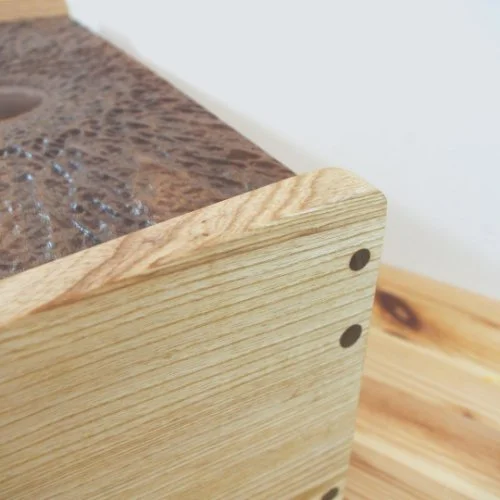 Close-up of a wooden box with Walnut dowels, showing part of a textured surface and a wooden surface.