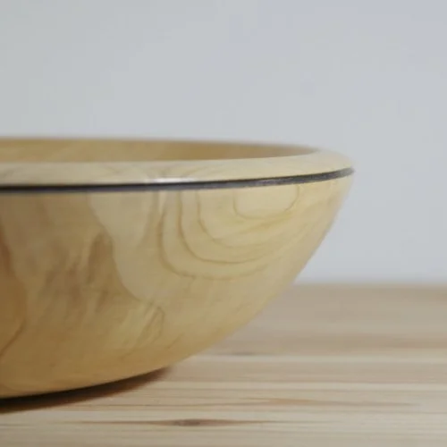 Close-up of a light-colored wooden bowl on a wooden surface with a plain gray background.