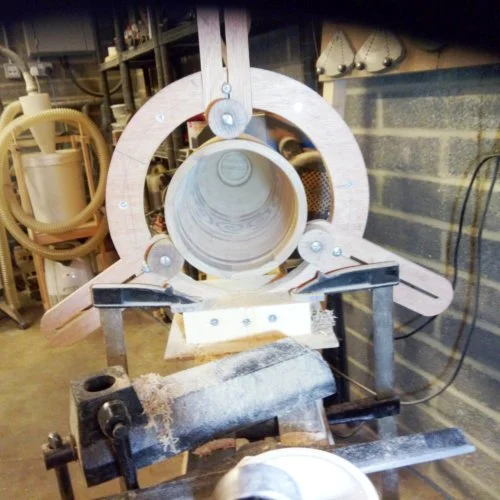 A woodworking lathe with a large wooden ring and a turned wooden piece in progress, positioned in a workshop.