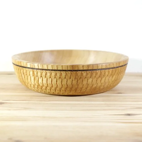 A round wooden bowl with a black stripe near the rim, sitting on a light wood surface.