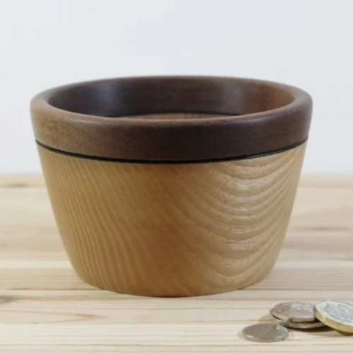 Wooden bowl on a light wooden surface with some coins nearby