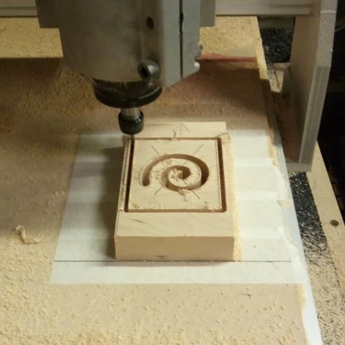 A CNC machine carving a spiral pattern into a wooden block.