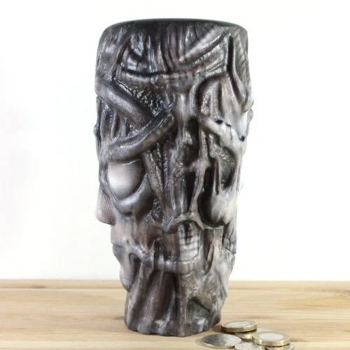 A wooden vase inspired by H.R.Giger, placed on a wooden surface with some coins at the base.