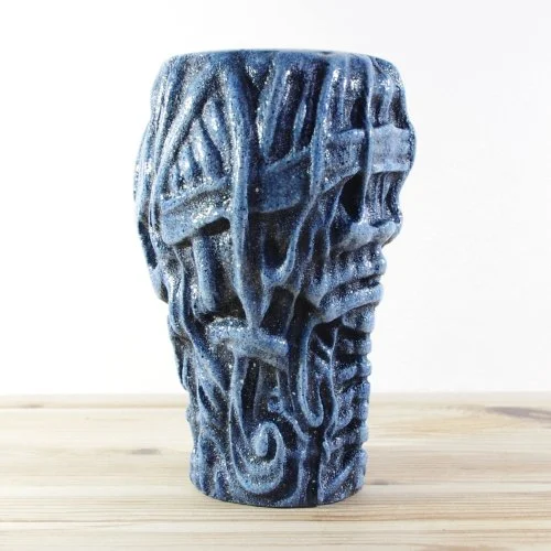 Blue wooden vase  with intricate abstract skull carved design, placed on a light wooden surface.