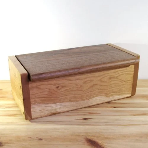Ash wooden storage box with a Walnut top, light wood sides, and a natural wood front, sitting on a wooden surface.