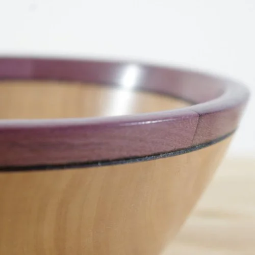 Close-up of a wooden bowl with a purple rim and black decorative line, showing part of its curved edge.