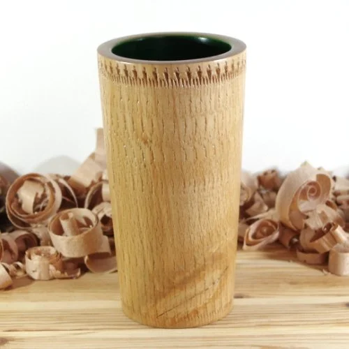 A wooden vase with a green interior, placed on a wooden surface with wood shavings in the background.