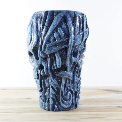 A blue wooden vase with an intricate carved pattern, placed on a wooden surface against a white background.