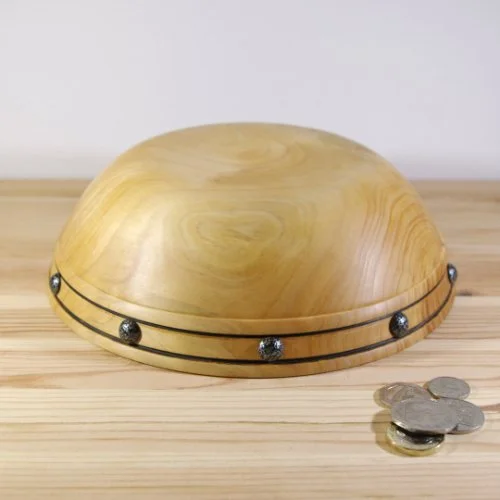 A wooden bowl with metal decorative elements and a few coins placed nearby on a wooden surface.